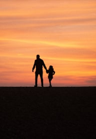A silhouette of a man and a child holding hands against a sunset.