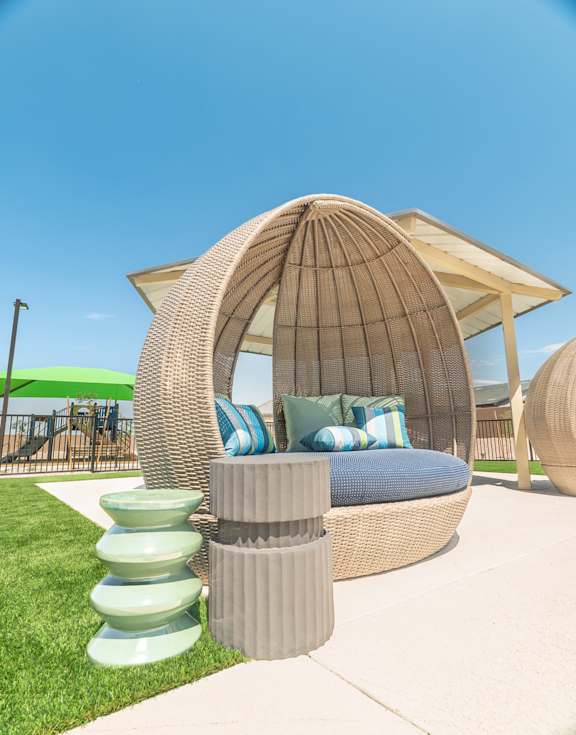 A large wicker outdoor chair with a cushion and a stack of plates on the side.