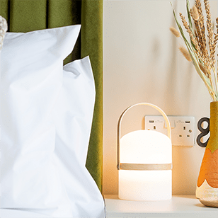 a nightstand with a white lamp and a pillow and a vase of flowers