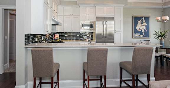 a kitchen with white cabinets and a bar with chairs
