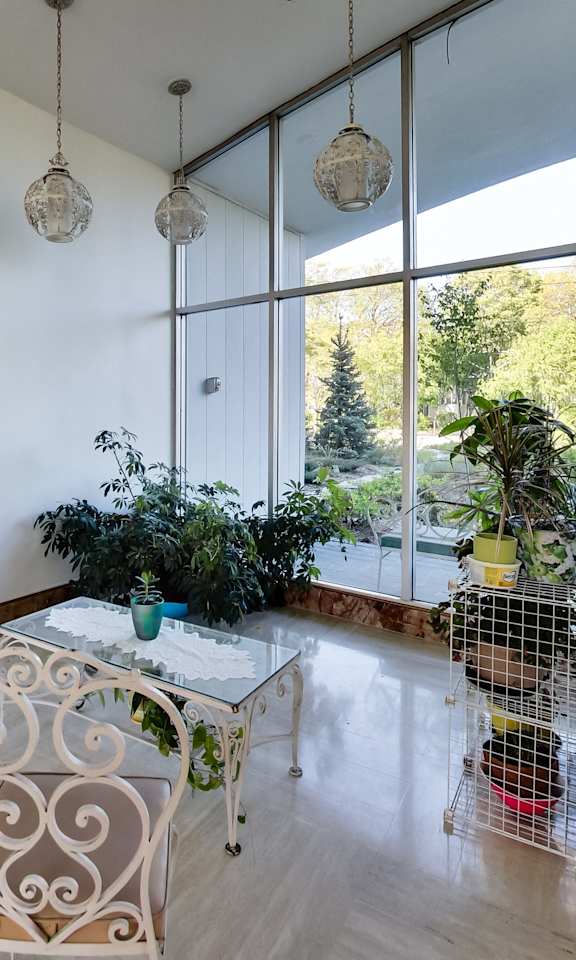 A white chair with a brown cushion is in a room with a table and plants.
