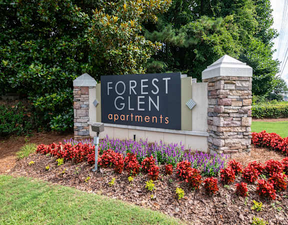 a sign for forest glen apartments in front of a flower garden