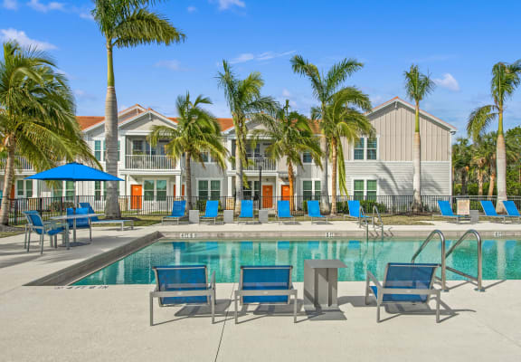 a swimming pool with blue chaise lounge chairs and palm trees in front of a building
