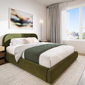 A bedroom with a green bed and a white nightstand.