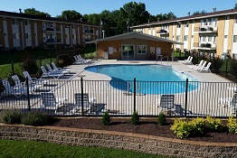 A pool surrounded by chairs and a building in the background.