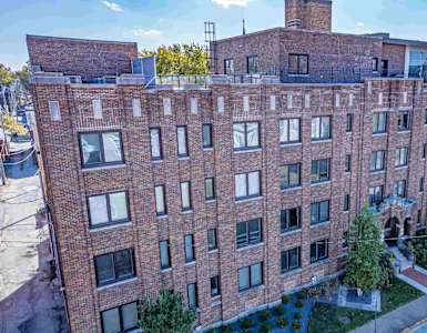 A large red brick building with a flat roof and a chimney on the top floor.