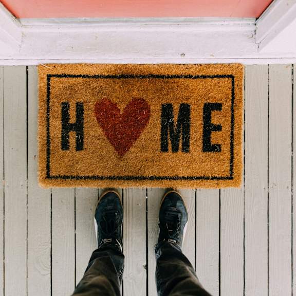 A person standing by a doormat that says "HOME" with a red heart.