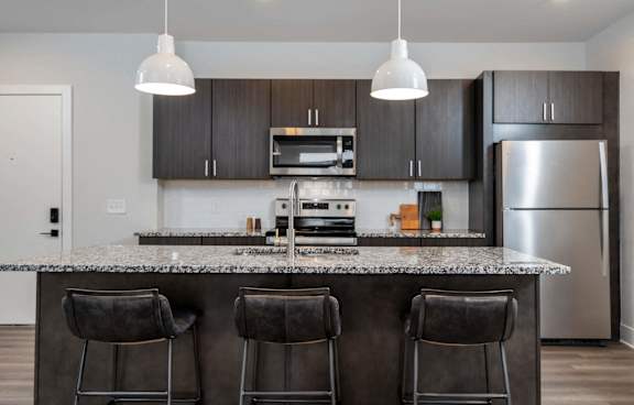 A modern kitchen with a granite countertop and bar stools.