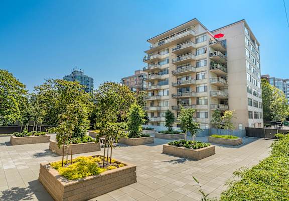 A modern apartment building with a courtyard garden in the foreground.