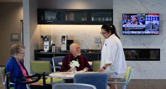 a nurse is talking to two patients in a dining room with tables and chairs