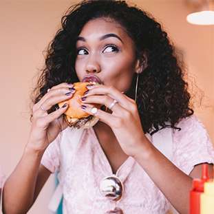 A woman with curly hair eating a burger.
