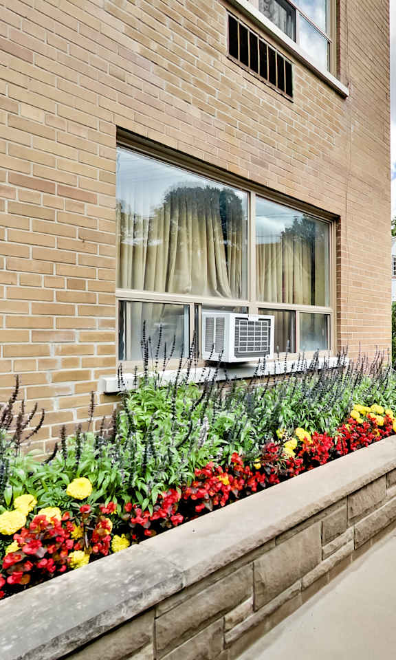 a side view of a brick building with a flower garden on the sidewalk