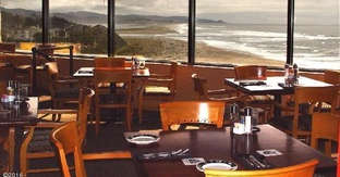 A restaurant with wooden chairs and tables overlooking the ocean.
