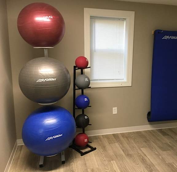 A set of exercise balls of different sizes and colors are on a stand in a room.