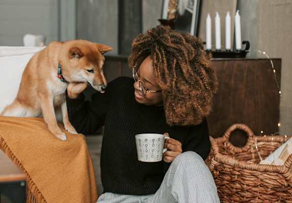 A person is sitting on the floor with a cup in hand and a dog on their lap.