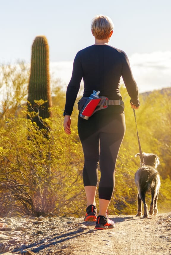 a woman walking her dog on a trail in the desert
