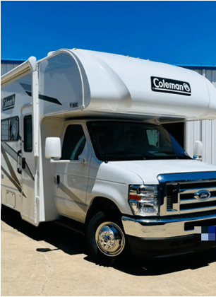 A white Coleman camper is parked in front of a building.