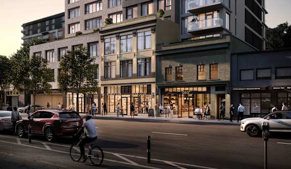 A street view of a modern apartment building with cars, a cyclist and buildings.