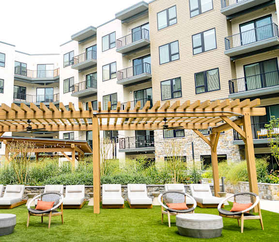an outdoor lounge area with lounge chairs and a pergola in front of an apartment building
