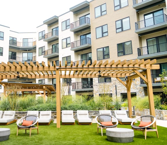 an outdoor lounge area with lounge chairs and a pergola in front of an apartment building