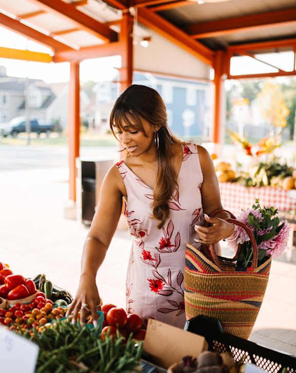 A woman in a floral dress is shopping for produce at an outdoor market.