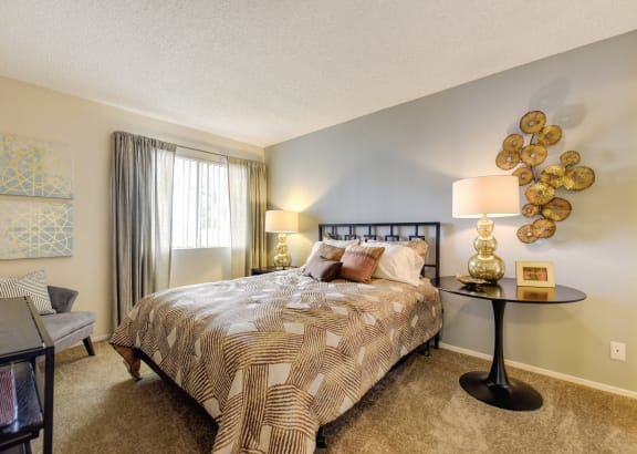 Model home bedroom with larger bed, side tables with decorative wall art. There is plush carpeting in the bedroom and a large window