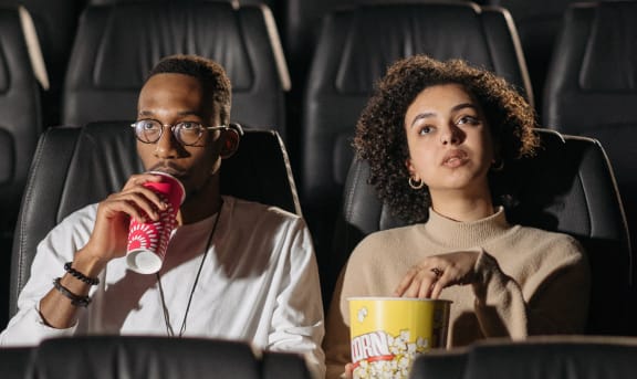 two people sitting in a movie theater eating popcorn and drinking soda