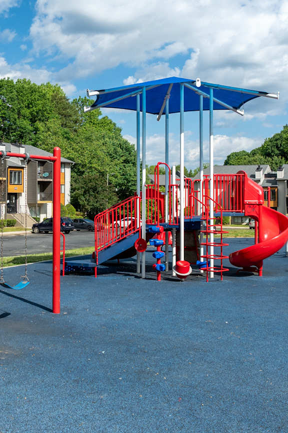 A playground with a red swing set and a blue umbrella.