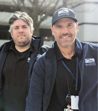 two men in black shirts and caps smiling at the camera