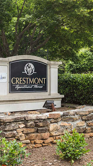 A sign that says Crestmont Apartment Homes in front of a stone wall.