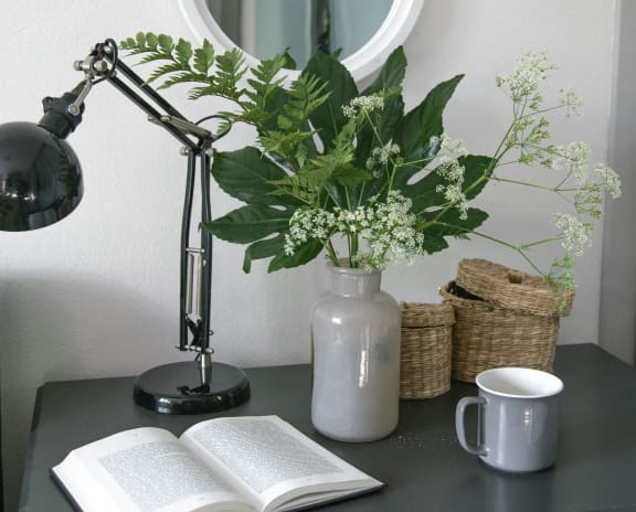 a vase with flowers on a table with an open book and a lamp