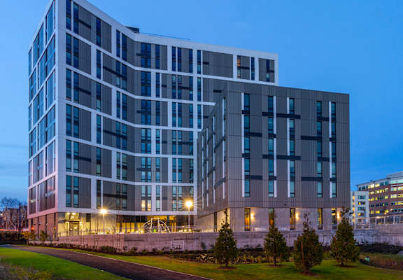 A modern building with a curved facade and multiple windows is illuminated from within.