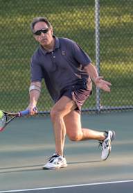 A man in a blue shirt and sunglasses is playing tennis.