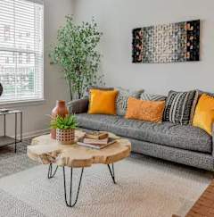 A living room with a grey couch, a round table with a plant on it, and a painting on the wall.