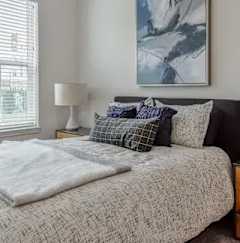 A bed with a white comforter and a grey pillow is in front of a painting.