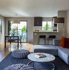 A living room with a grey couch, a round table with a book on it, and a grey knitted pouf.