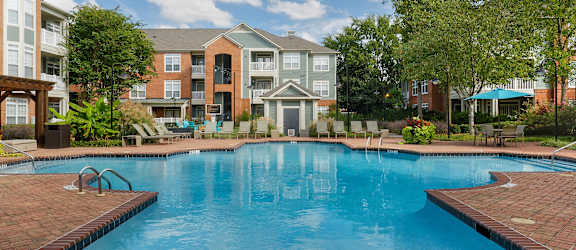 A large swimming pool surrounded by a brick patio and residential buildings.
