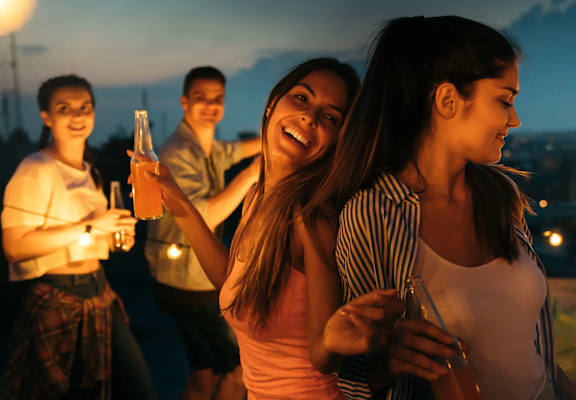 Four friends are enjoying a night out on a rooftop with drinks in hand.