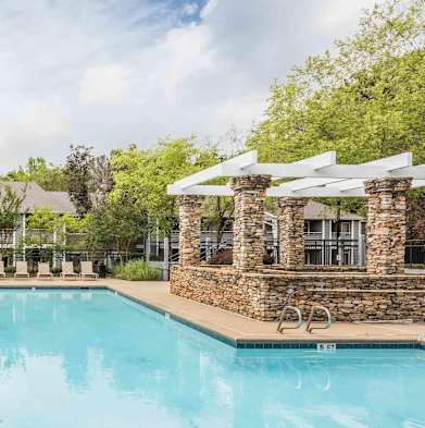 A swimming pool surrounded by trees and a stone building.