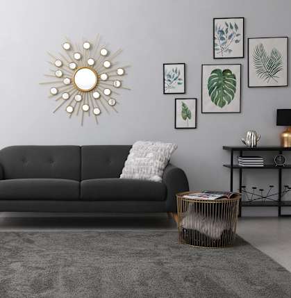 a living room with a black couch and a sun clock on the wall