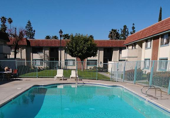 a pool with a fence around it and apartment buildings in the background