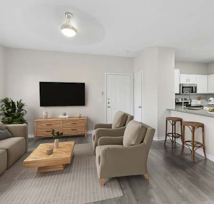 A modern living room with a grey sofa, a wooden coffee table, and a kitchen area in the background.