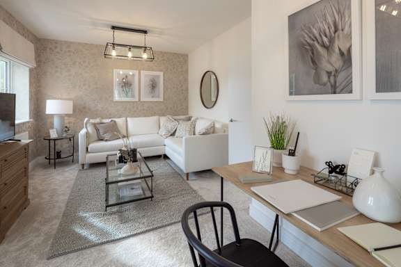 A modern living room with a white sofa, a glass coffee table, and a wooden desk.