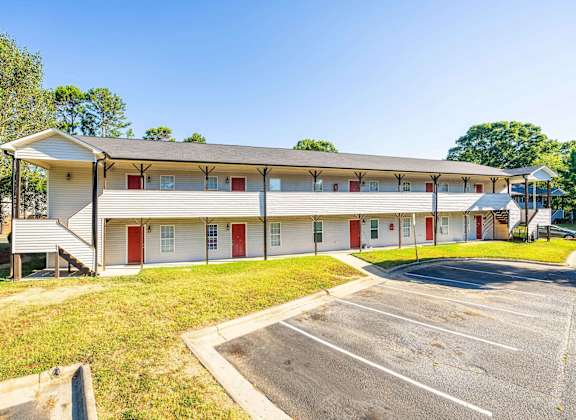 a large white building with red doors and a parking lot at Ashford Place Apartments, Kannapolis, NC
