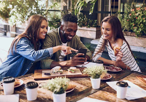 Three people are sitting at a table with food and drinks, enjoying a meal together.