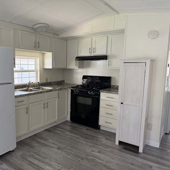 A white refrigerator stands in a kitchen with wooden floors and white cabinets.
