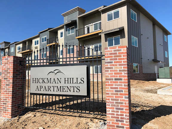 A sign for Hickman Hills Apartments in front of an apartment building.