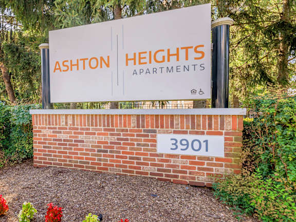 A sign for Ashton Heights Apartments with a brick wall and flowers in the foreground. at Ashton Heights Apartments, Suitland, MD