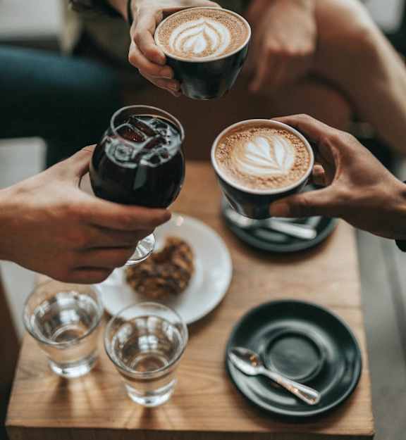 A group of people toasting with cups of coffee and a glass of soda.