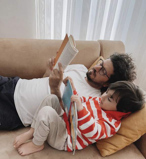 A man and a child are reading a book together on a couch.